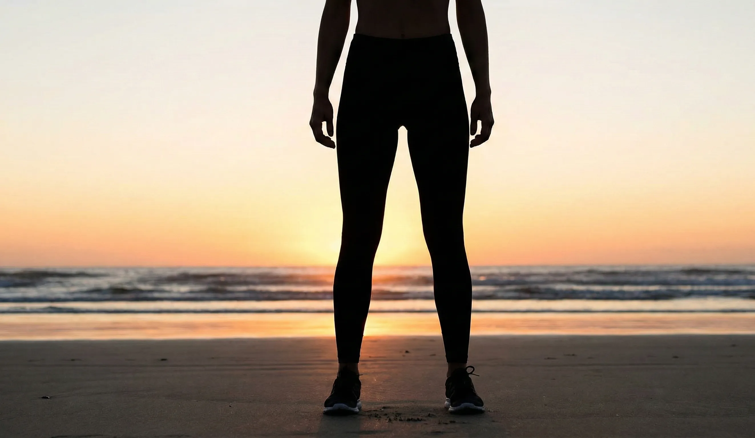 natural silhouette of fit woman with thigh gap on beach at sunset