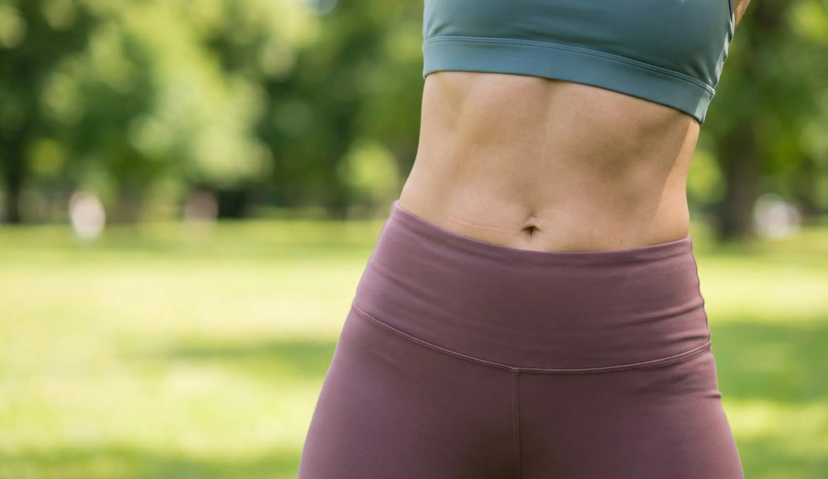 healed tummy tuck scar on fit woman in park
